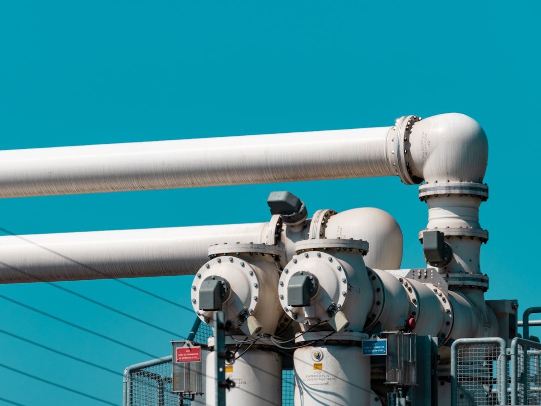 A pair of white-painted wellhead valves and pipework set against a clear sky