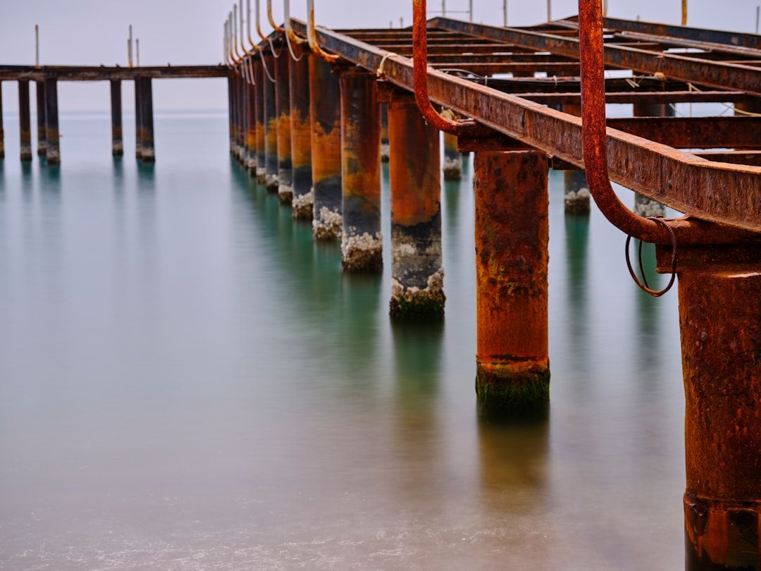 Heavily corroded steel pier pilings rising from calm coastal water